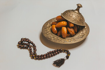 Bronze plate with dates and wooden rosary on a light background. Ramadan background. Ramadan kareem.
