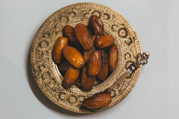 Bronze plate with dried dates and spoon, close-up. Ramadan Kareem holiday concept