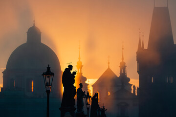 Statues on Charles Bridge against urban skyline with church and towers.  Beautiful sunrise in...
