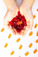 Many gummy bears in the chld hands. Child holds in hands vitamins gummy bears on white background. Medical concept.  Top view, flat lay. 