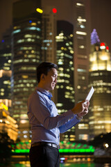 Chinese businessman outdoors at night using his digital tablet device.