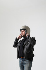 Stylish bearded young biker man wearing black jacket and helmet posing indoor. 