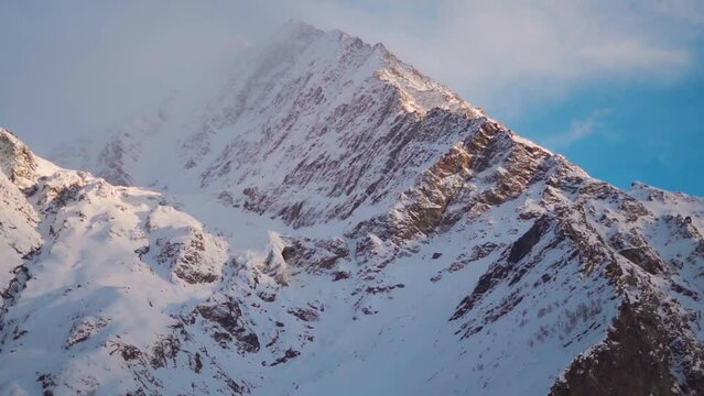Closeup shot of orange clouds above the snow covered Himalayan mountain peaks during sunset in the winter season at Lahaul Valley in Himachal Pradesh, India. View of Himalayan mountains in sunset.