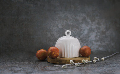 Festive Easter spring composition with white ceramic tea pair and red eggs on wooden podium with willow branch and handmade paper rabbit on dark background