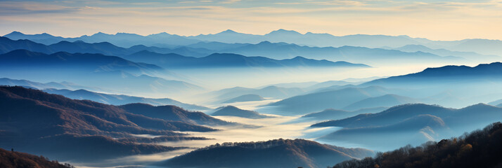 Fototapeta premium Panoramic view of a mountainous landscape enshrouded in the soft mist of early morning. Various shades of blue and grey layered effect. Light and shadow adds sense of tranquility to the scene.