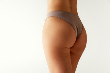 Rear view of female body, legs, buttocks in neutral-tone underwear against grey studio background. Body positivity. Concept of beauty treatments, dieting, female health, spa procedures. Ad
