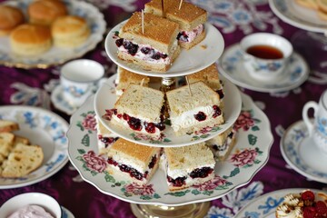 Elegant afternoon tea party, with tiered trays of finger sandwiches, scones with clotted cream and jam, and delicate petit fours.