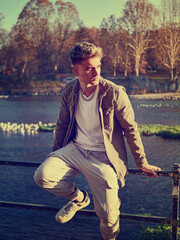 A man is leaning casually on a rail near a body of water, with a relaxed posture. The scene...