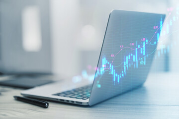 A sleek laptop projecting a virtual stock market chart, with pen and blurred background