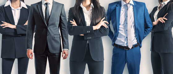 A group of five corporate professionals in suits standing confidently with arms crossed It...
