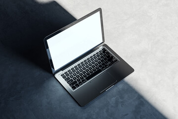 Sleek laptop with blank white screen on a concrete surface, highlighted by natural light. Product...