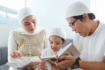 Portrait of happy muslim family with a child reading Al-Quran and pray together at home