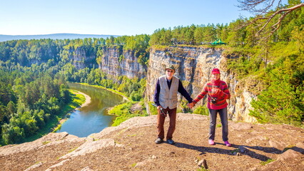 a beautiful mature couple on a high rock admires the Ural nature and the Ai river on a summer sunny...