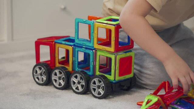 little boy playing with magnetic tiles stacking blocks game set toy. Child building car from blocks.