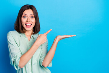 Photo of impressed woman dressed turquoise shirt indicating at awesome product on palm empty space isolated on blue color background