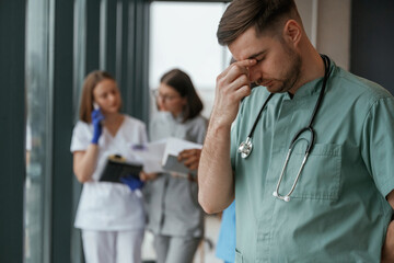 Guy is feeling bad. Group of doctors are together indoors - obrazy, fototapety, plakaty