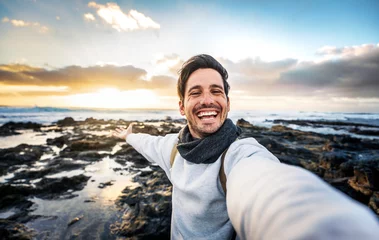 Photo sur Aluminium les îles Canaries Handsome young man taking selfie pic with smart mobile phone outdoors - Traveler guy smiling at camera with sunset on background - Traveling life style and technology concept