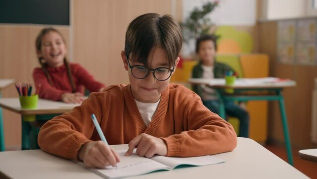 Angry playful noisy children classmates schoolgirl girl kid schoolboy child throw crumpled papers balls in little guy boy in glasses nerd writing task copybook bulling in primary school class lesson