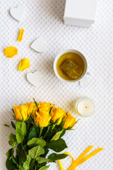 Eine Teetasse, ein gelber Rosenstrauss und Herzen auf einer weißen Wolldecke. Hygge, Muttertag.