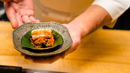 Sushi chef serving Red King Crab sashimi with crab's eggs in Omakase restaurant.