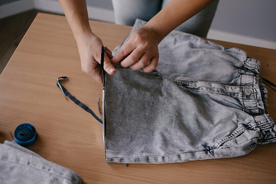 Denim Upcycling Ideas, Using Old Jeans, Repurposing Jeans, Reusing Old Jeans, Upcycle Stuff. Woman seamstress cut and repair old blue jeans in sewing studio.