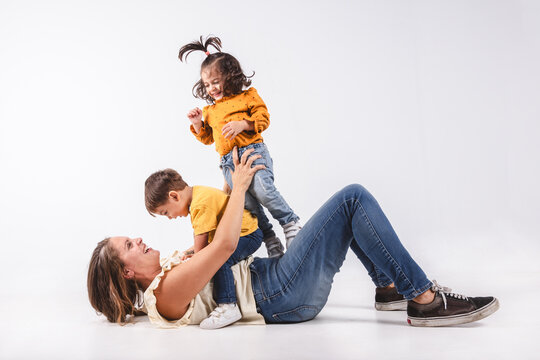 A mother lying on the floor holds her two children playing on white background