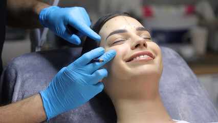 A cosmetologist marks with a pen the site of a beauty injection in the forehead of a beautiful patient. Concept of preparing for an injection of a beautiful young woman.