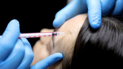 A cosmetologist gives a beauty injection to a woman's face in a cosmetology center, close-up....