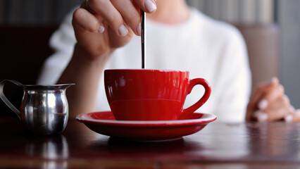 The hands of an unrecognizable woman in a stylish modern cafe mix sugar with tea or coffee. Concept of morning breakfast, small business and cozy atmosphere.