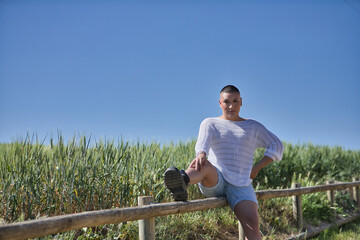 Non-binary person, young and South American, heavily makeup, sitting on a wooden fence, next to a...