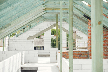 Wooden roof framing. Unfinished roof trusses and aerated concrete block walls, view in attic with rafters and beams. Modern farmhouse building construction.