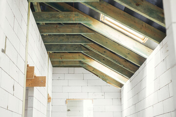 Unfinished attic wooden roof framing with vapor barrier, dormer and windows. View on timber rafters...