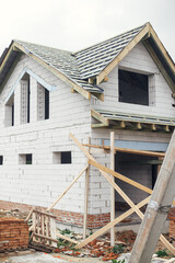Fototapeta na wymiar Unfinished house. Wooden roof framing with vapor barrier and dormer on block walls with windows. New modern farmhouse construction. Timber trusses Rafters and beams on aerated concrete blocks