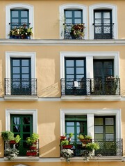 Fototapeta na wymiar Cozy facade of warm colours with simple windows and balconies with flowers downtown Madrid, Spain. Vertical photo