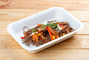 Buckwheat noodles with vegetables. Vegetarian food. Takeaway food. On a wooden background.
