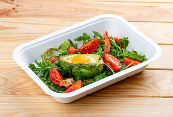 Baked egg in avocado with lettuce and tomatoes. Healthy diet. Takeaway food.  On a wooden background.