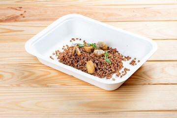 Buckwheat porridge with mushrooms. Healthy food. Takeaway food.  On a wooden background.