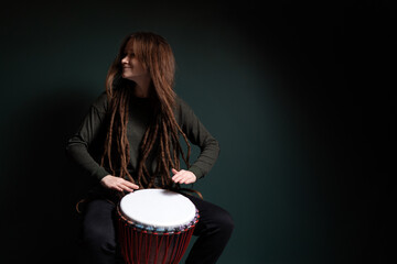 Percussion musician. Pretty young woman playing djembe. Green background.