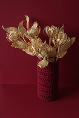 Flowers made of straw on a red background in a knitted vase. Straw weaving