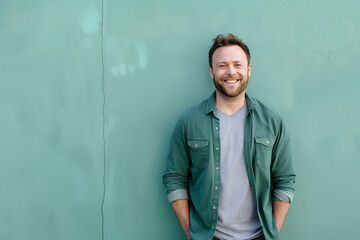 Obraz premium Joyful Man with a Beard Smiling Confidently in Green Shirt, Leaning Against a Textured Wall