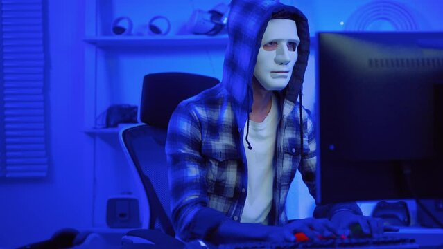hacker wearing a white mask is using a computer to steal confidential information.Concepts: computer crime, burglary, business security on computer networks

