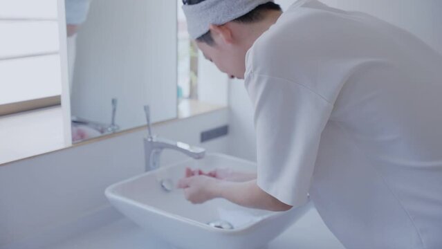 洗面所で洗顔する若い男性