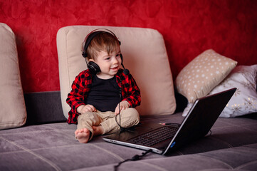An engrossed toddler wearing headphones sits in front of a laptop, a glimpse into the modern...