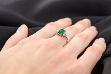 Beautiful female hand with gold ring with diamonds and emerald on gray background