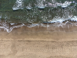 Drone view of the sandy beach and the waves on the sea on a sunny day, top view. Summer seascape from the air. Concept and idea of travel