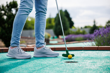 Golfer playing adventure or mini golf and trying putting ball into hole. Sports and leisure activity - obrazy, fototapety, plakaty