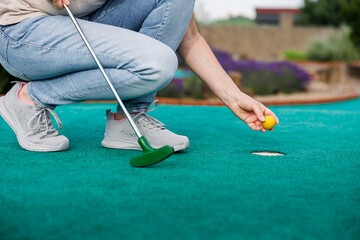 Woman plays mini golf and taking ball out from the hole after successful putting