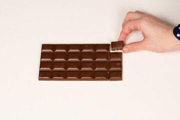 Woman's hand grabs a piece of chocolate, chocolate bar on a white background