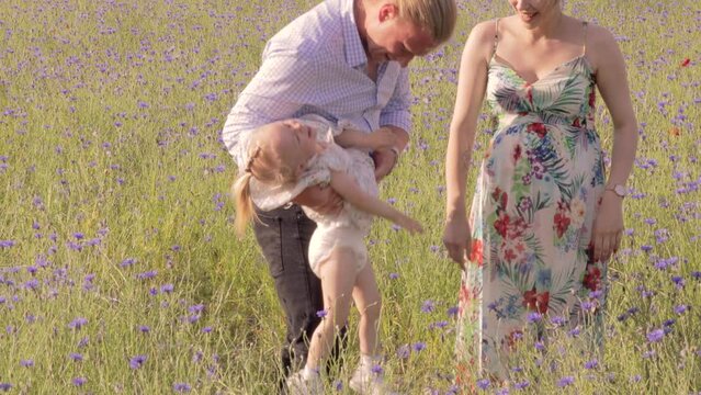 Adorable scene of parents tickling their toddler daughter in a flower field