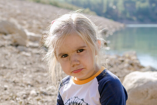 Little girl with blond hair looking at the camera with a sad expression on her face.